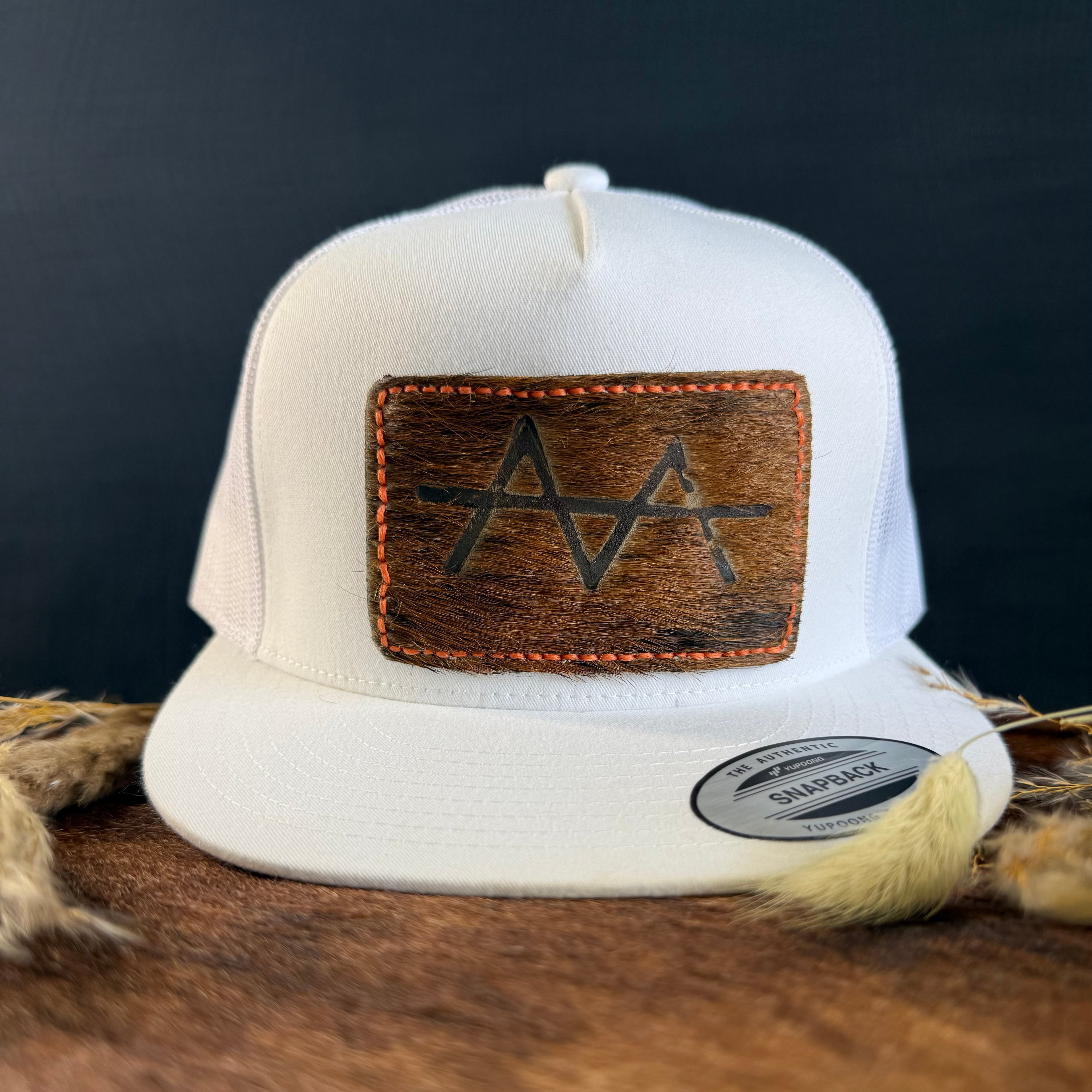 White snapback hat with dark cowhide patch and coral hand-stitched border, branded with a registered cattle brand