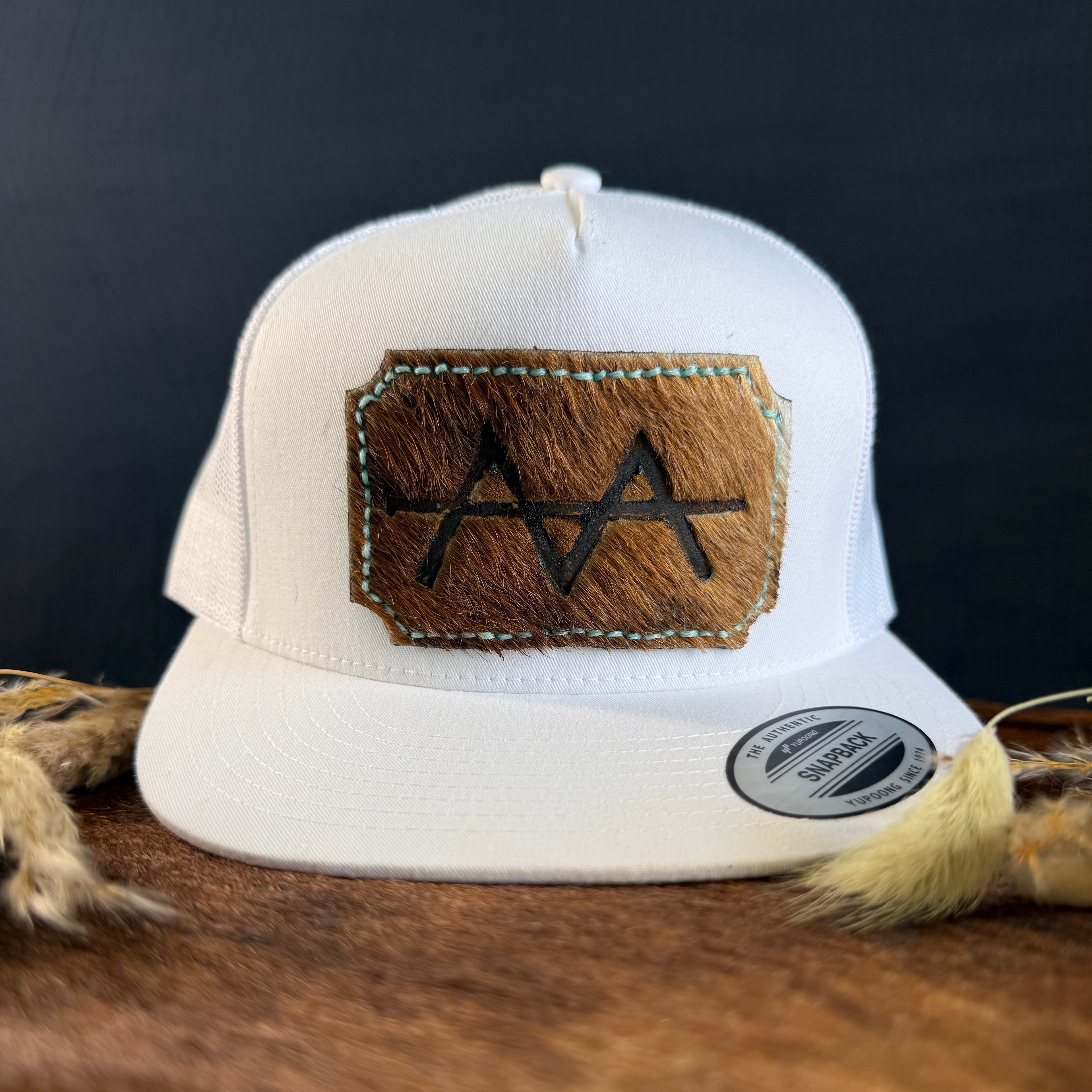 White snapback hat with warm brown scalloped cowhide patch and mint turquoise hand-stitched border, branded with a registered cattle brand