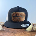 Black and white trucker snapback hat with scalloped espresso cowhide patch and olive gold tonal stitched border, branded with a registered cattle brand