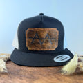 Black and white trucker snapback hat with scalloped warm brown cowhide patch and orange hand-stitched border, branded with a registered cattle brand