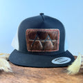 Black and white trucker snapback hat with deep espresso cowhide patch and red hand-stitched border, branded with a registered cattle brand