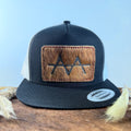 Black and white trucker snapback hat with golden tan brindle cowhide patch and red hand-stitched border, branded with a registered cattle brand