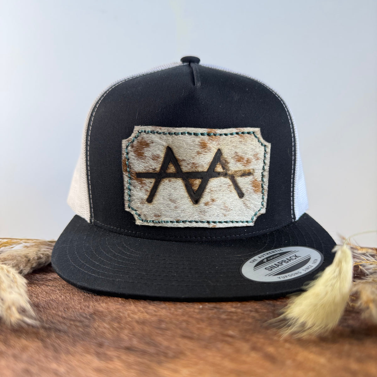 Black and white trucker snapback hat with scalloped pale cream and gold speckled cowhide patch and mint green hand-stitched border, branded with a registered cattle brand