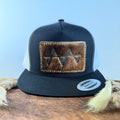 Black and white trucker snapback hat with dark brindle cowhide patch and tan tonal stitched border, branded with a registered cattle brand