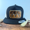 Black and white trucker snapback hat with scalloped medium brown brindle cowhide patch and cream tonal stitched border, branded with a registered cattle brand