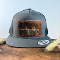 Charcoal grey snapback hat with dark brindle cowhide patch and red hand-stitched border, branded with a registered cattle brand