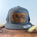 Charcoal grey snapback hat with scalloped golden brindle cowhide patch and gold tonal stitched border, branded with a registered cattle brand