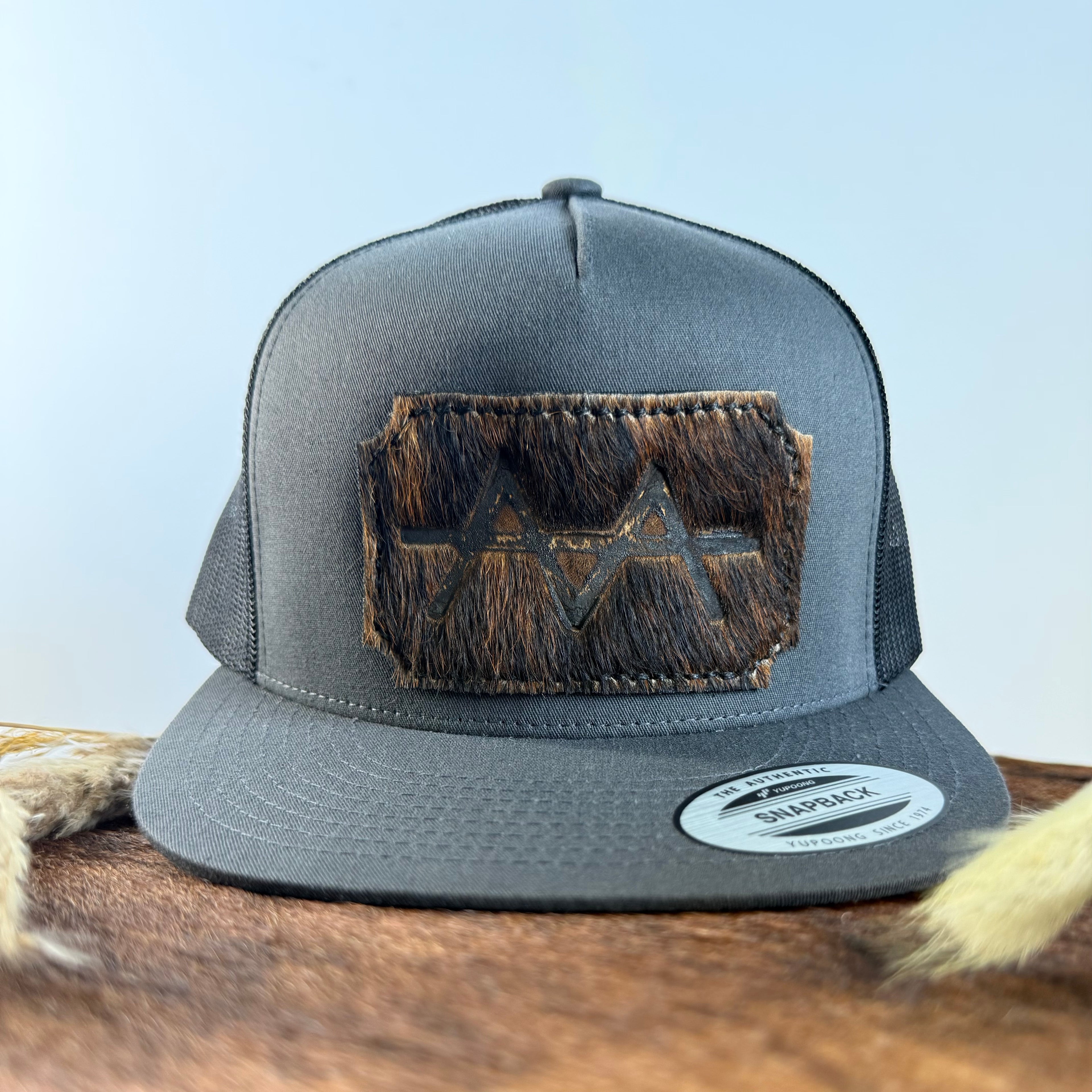 Charcoal grey snapback hat with near-black brindle cowhide patch and tonal dark stitched border, branded with a registered cattle brand