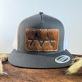 Charcoal and white trucker snapback hat with golden brown cowhide patch and blush rose hand-stitched border, branded with a registered cattle brand