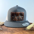 Charcoal and white trucker snapback hat with deep dark brindle cowhide patch and burgundy wine hand-stitched border, branded with a registered cattle brand