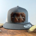 Charcoal and white trucker snapback hat with scalloped dark brindle cowhide patch and tonal dark stitched border, branded with a registered cattle brand