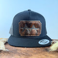 All-black trucker snapback hat with scalloped espresso brindle cowhide patch and tonal brown stitched border, branded with a registered cattle brand