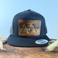All-black trucker snapback hat with golden brown brindle cowhide patch and copper tonal stitched border, branded with a registered cattle brand