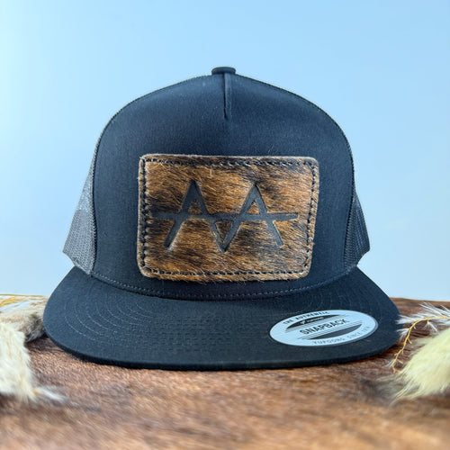 All-black trucker snapback hat with medium warm brindle cowhide patch and tonal dark stitched border, branded with a registered cattle brand