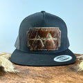 All-black trucker snapback hat with scalloped dark brindle cowhide patch and teal hand-stitched border, branded with a registered cattle brand